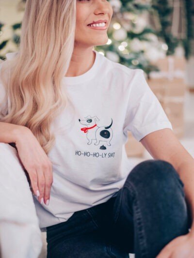 1. Woman sitting indoors wearing white T-shirt with dog graphic and 'Ho-ho-ho-ly sh*t' text, smiling