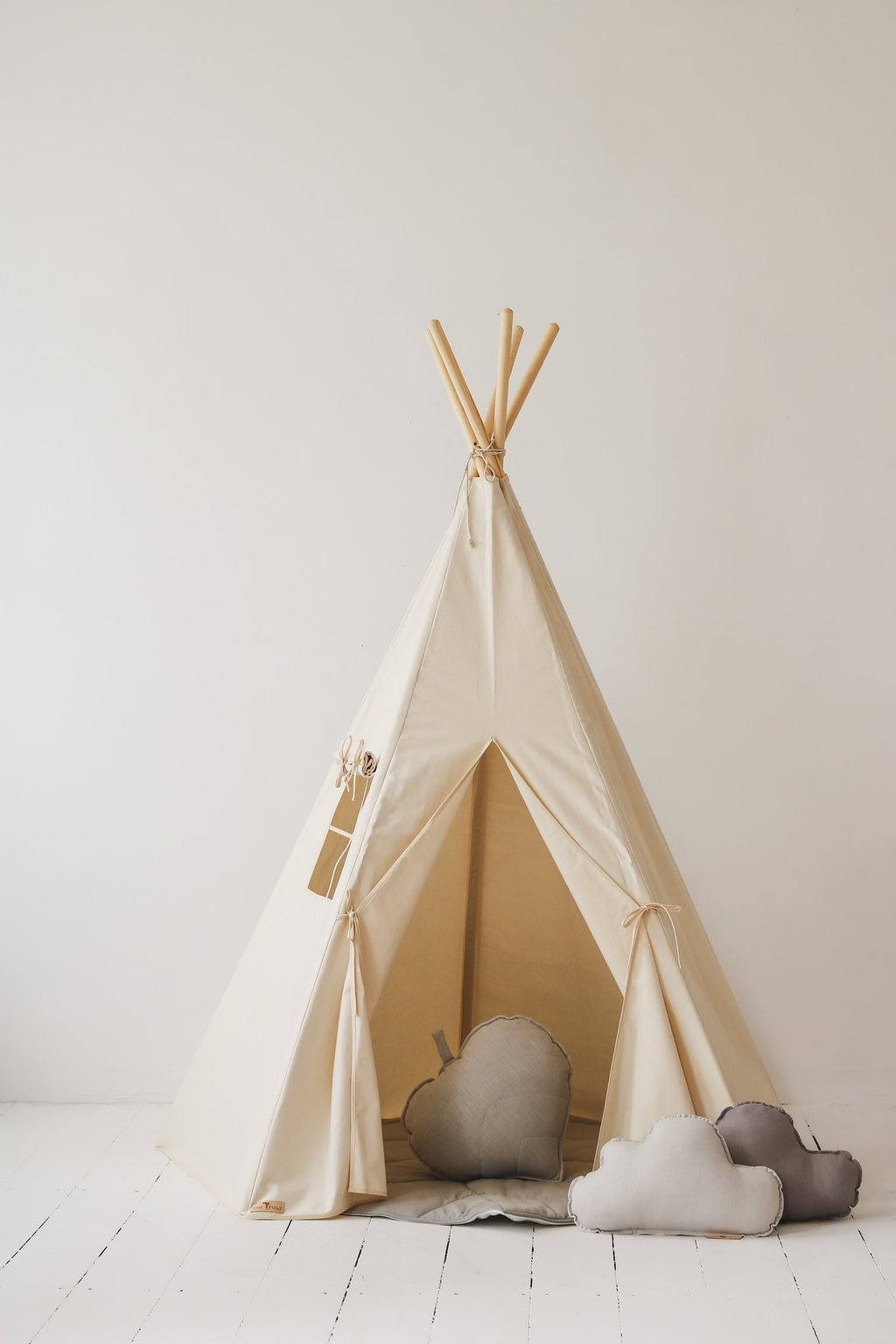 1. Beige teepee tent with window and open entrance, decorated with grey and white cloud cushions, in a studio setting