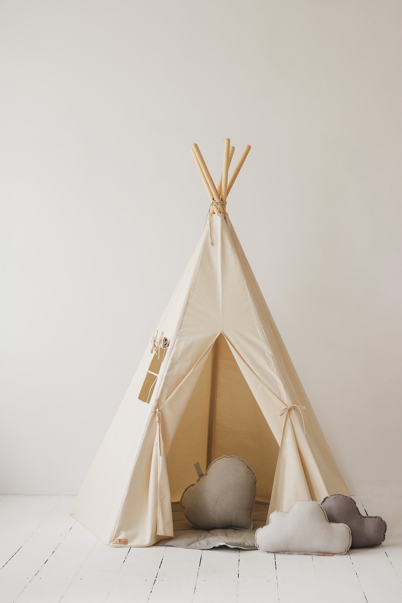 1. Beige teepee tent with window and open entrance, decorated with grey and white cloud cushions, in a studio setting