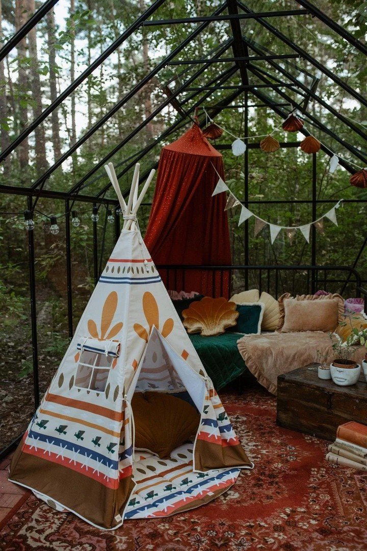 1. Indoor greenhouse setting with Moi Mili teepee tent featuring geometric prints, surrounded by cozy decor and plants