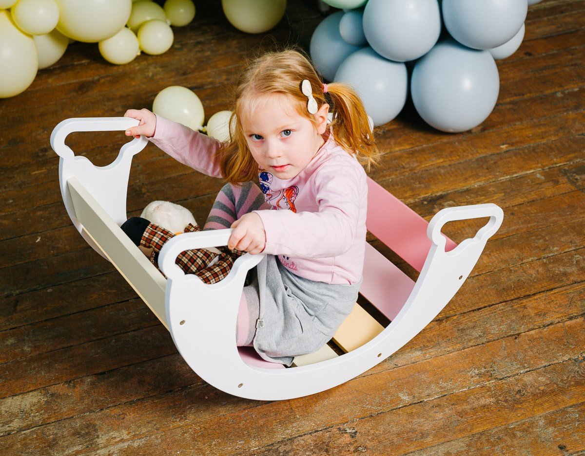 1. Child sitting inside colorful rainbow climber on wooden floor