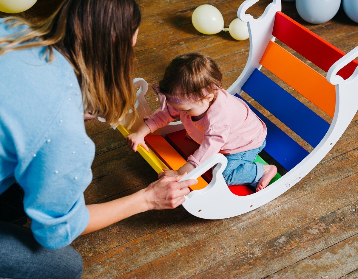 1. Child playing inside colorful rainbow climber with adult supervision