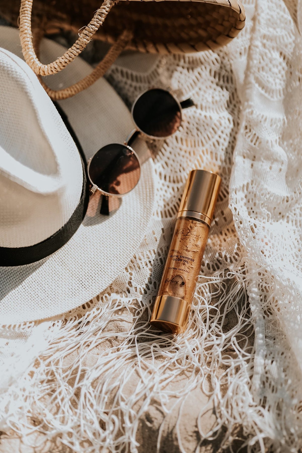 2. North Beauty Tinted Glow Oil bottle styled with summer accessories on a lace fabric