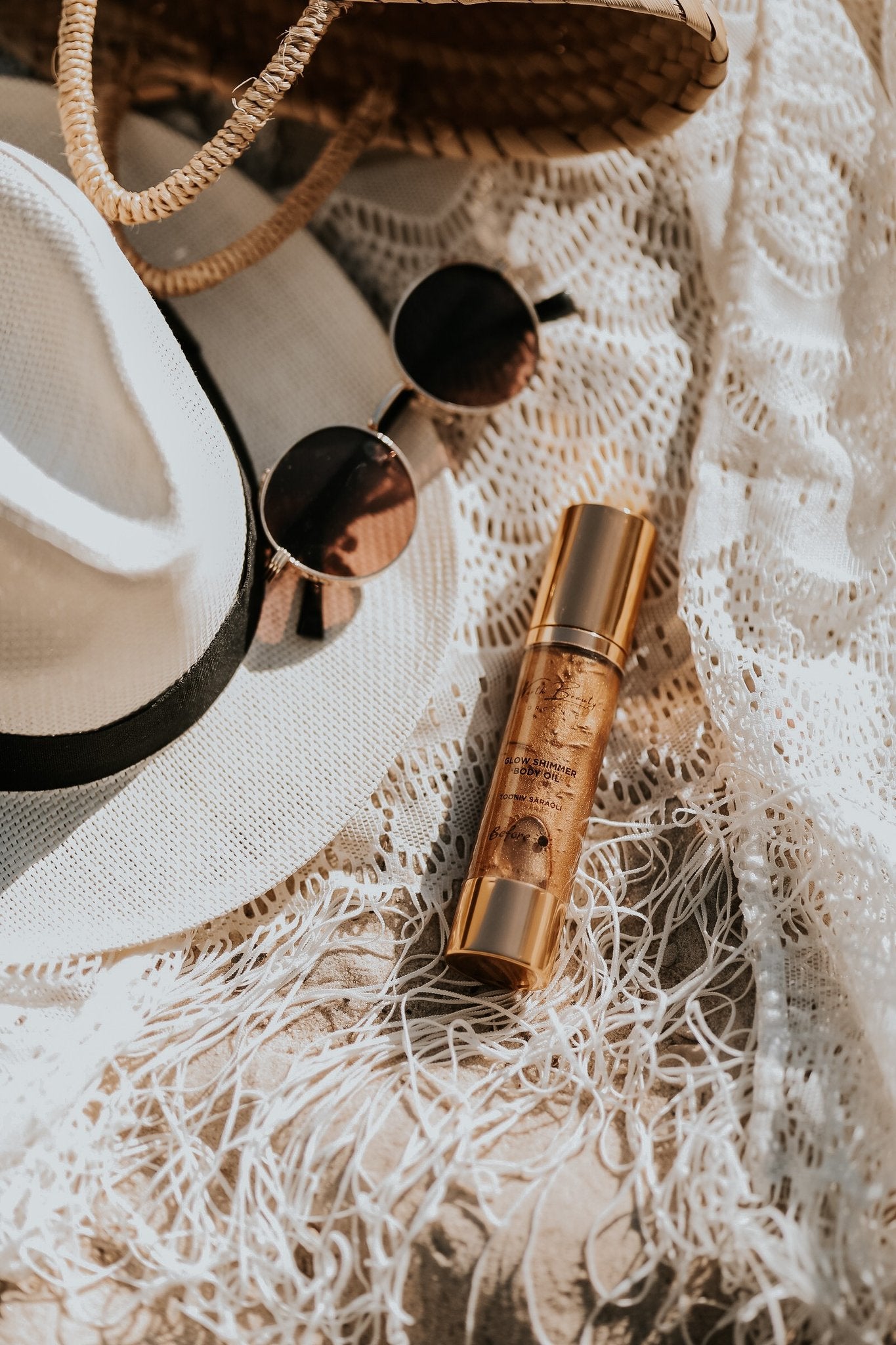2. North Beauty Tinted Glow Oil bottle styled with summer accessories on a lace fabric