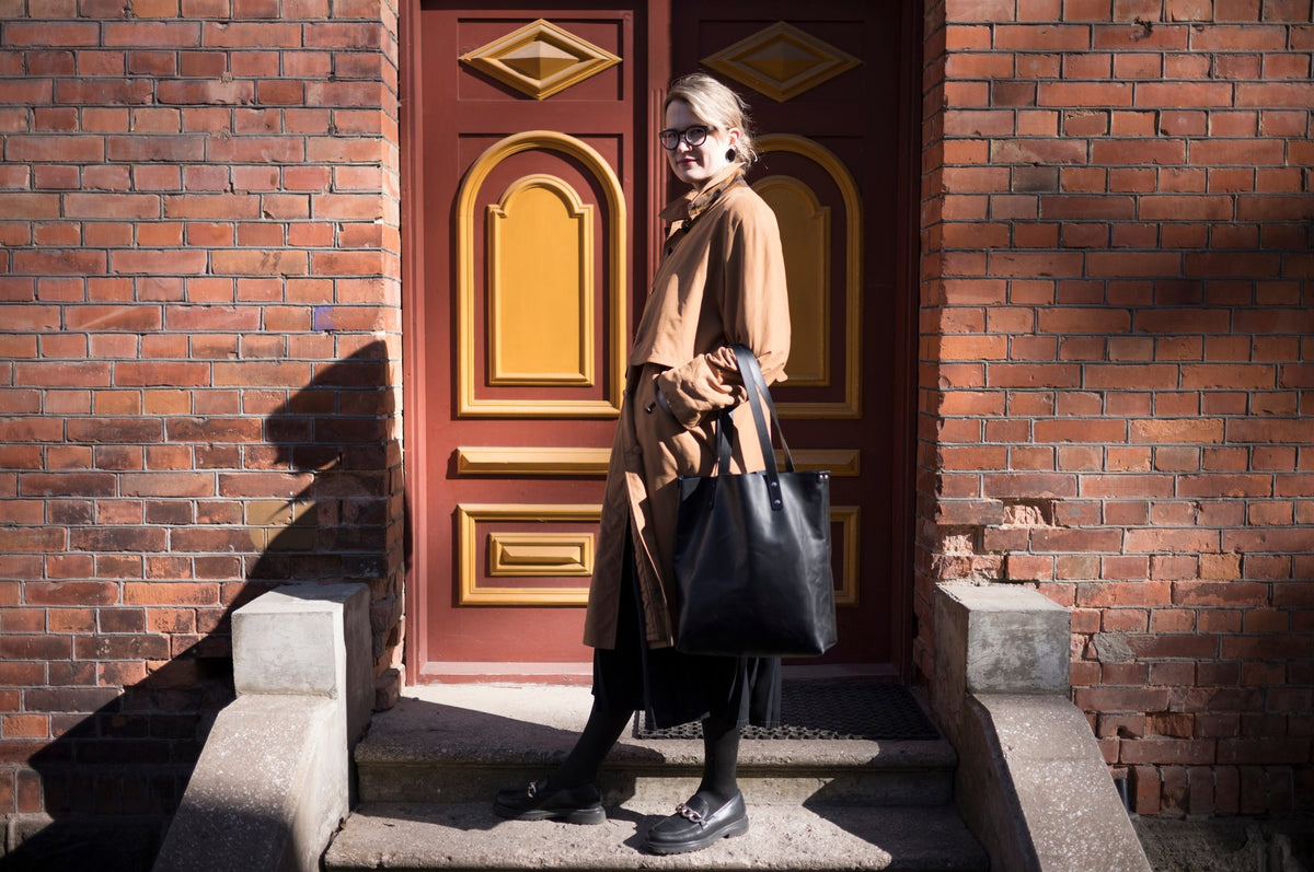 1. Woman in brown coat standing on steps with black Stella Soomlais tote bag in front of ornate door