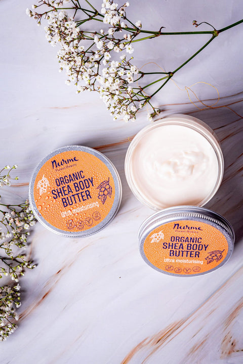 1. Open and closed Nurme shea body butter containers on marble surface with white flowers
