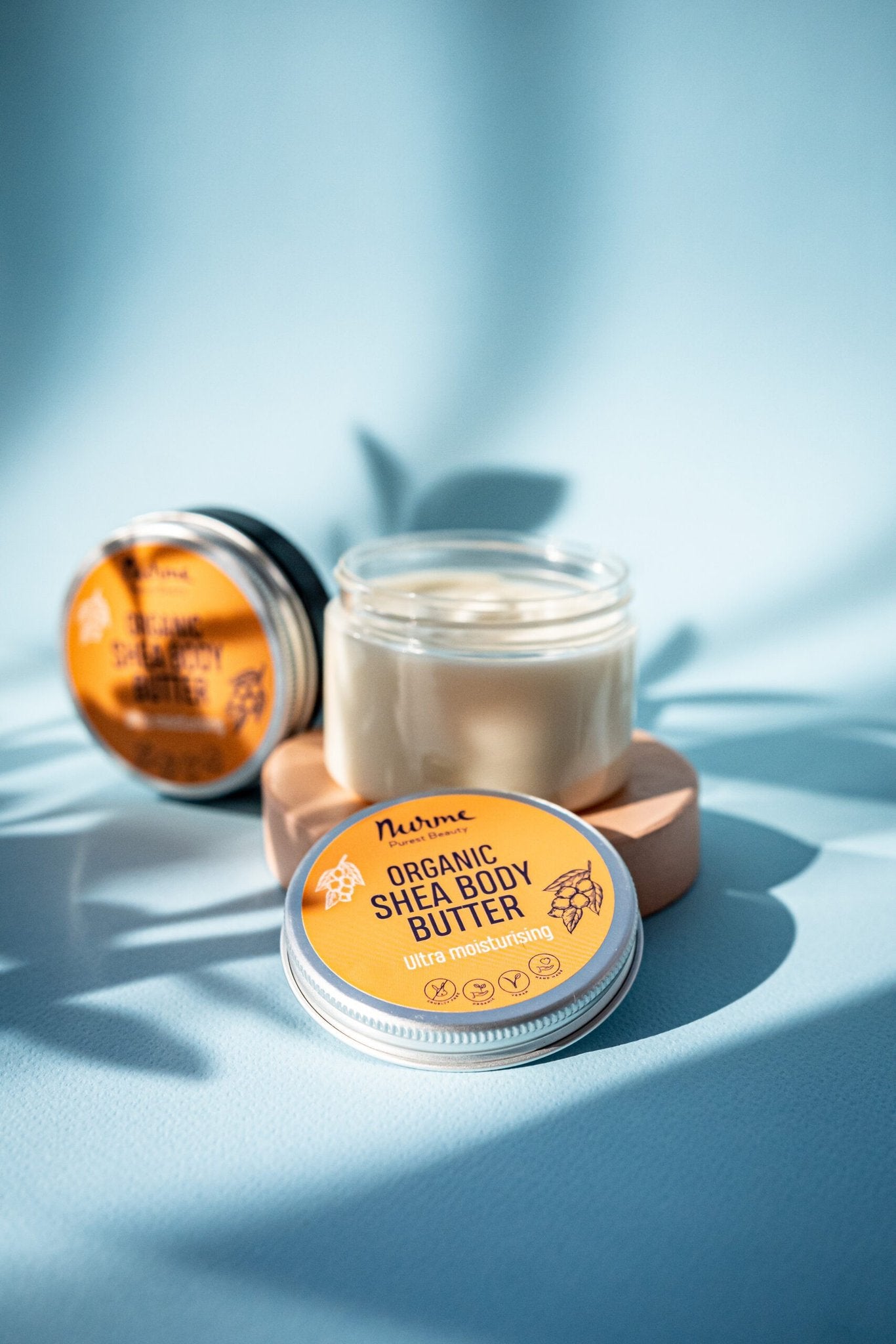 1. Open jar of Nurme Ultra Moisturising Shea Body Butter with lid and additional jar in background on blue surface