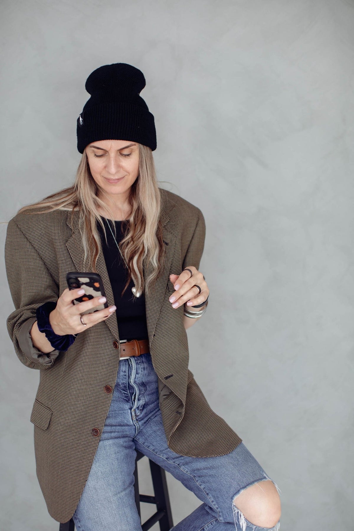 3. Woman wearing black beanie with giraffe label, seated and using smartphone, casual attire