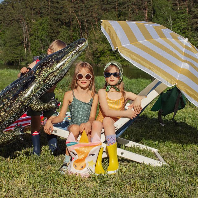 3. Two girls with MUNI Unicorn and crocodile backpacks under umbrella, emphasizing playful and adventurous style
