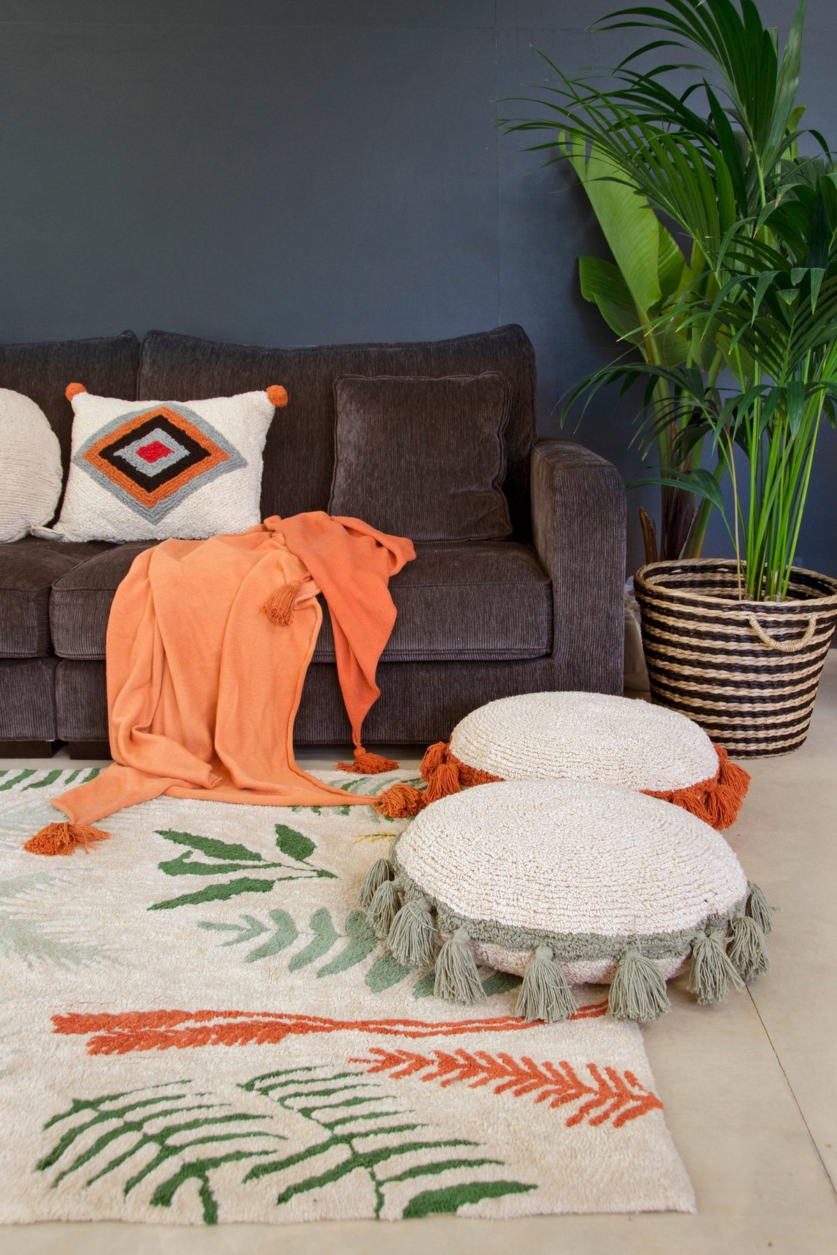 8. Botanical rug in a living room with a dark sofa, orange throw, and decorative cushions