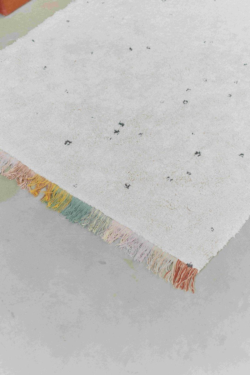 3. Close-up of Lorena Canals Stardust rug showing natural color, dark dots, and multicolored fringes