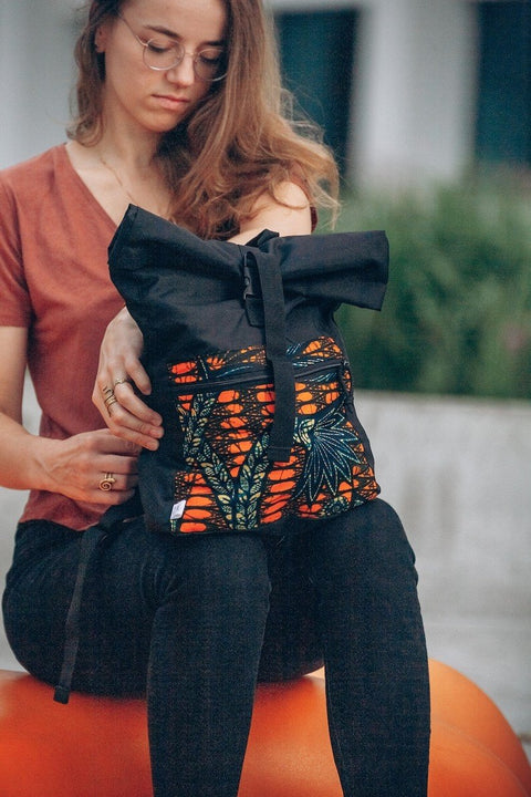 1. Woman sitting outdoors holding Drinbags waterproof rolltop backpack with vibrant yellow and orange pattern