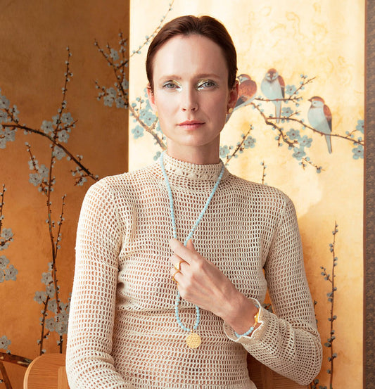 1. Woman wearing Hathor Harmony Bracelet in aquamarine and gold-plated silver by New Vintage by Kriss, styled with a beige knit top in a lifestyle setting