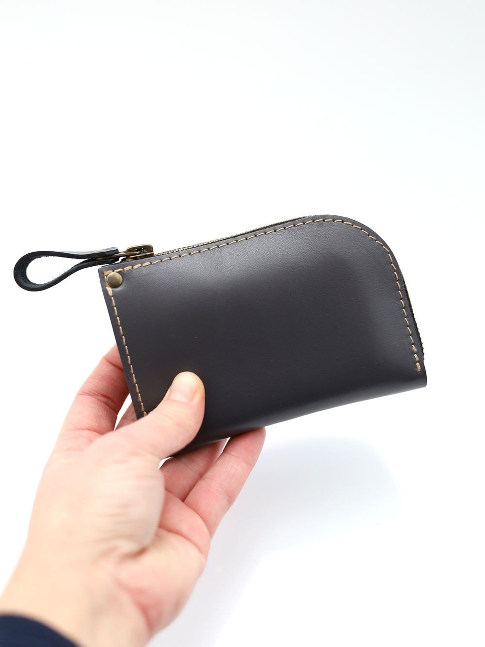 1. Person holding grey leather wallet by TOKS VISOKS with curved zipper and visible stitching