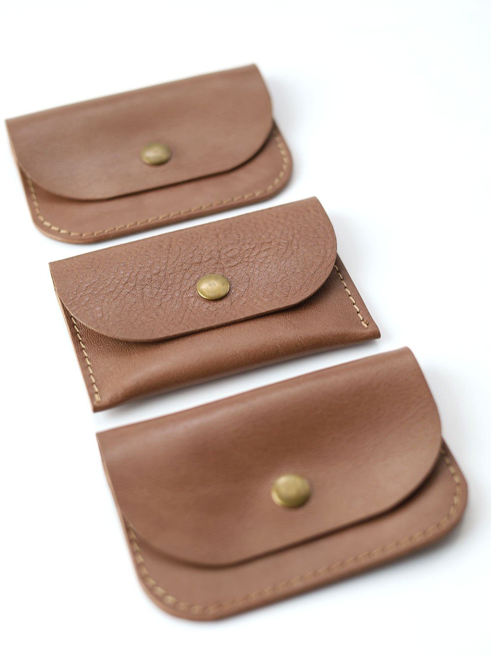 4. Flat lay of three Toks Visoks WEEKEND wallets in cappuccino leather with brass buttons