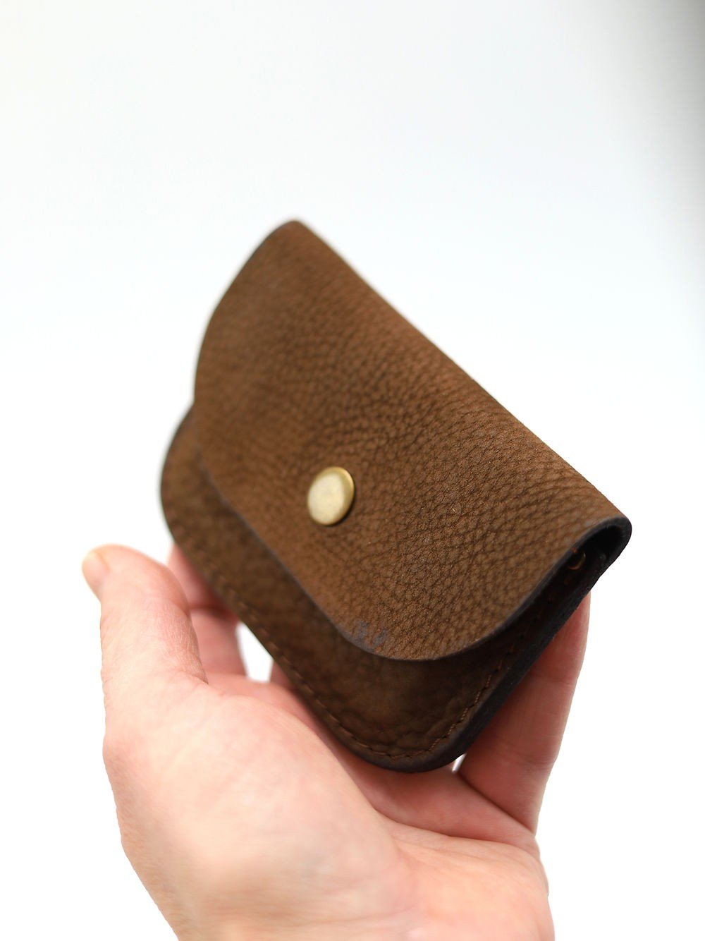5. Hand holding brown nubuck leather wallet with visible texture and brass button