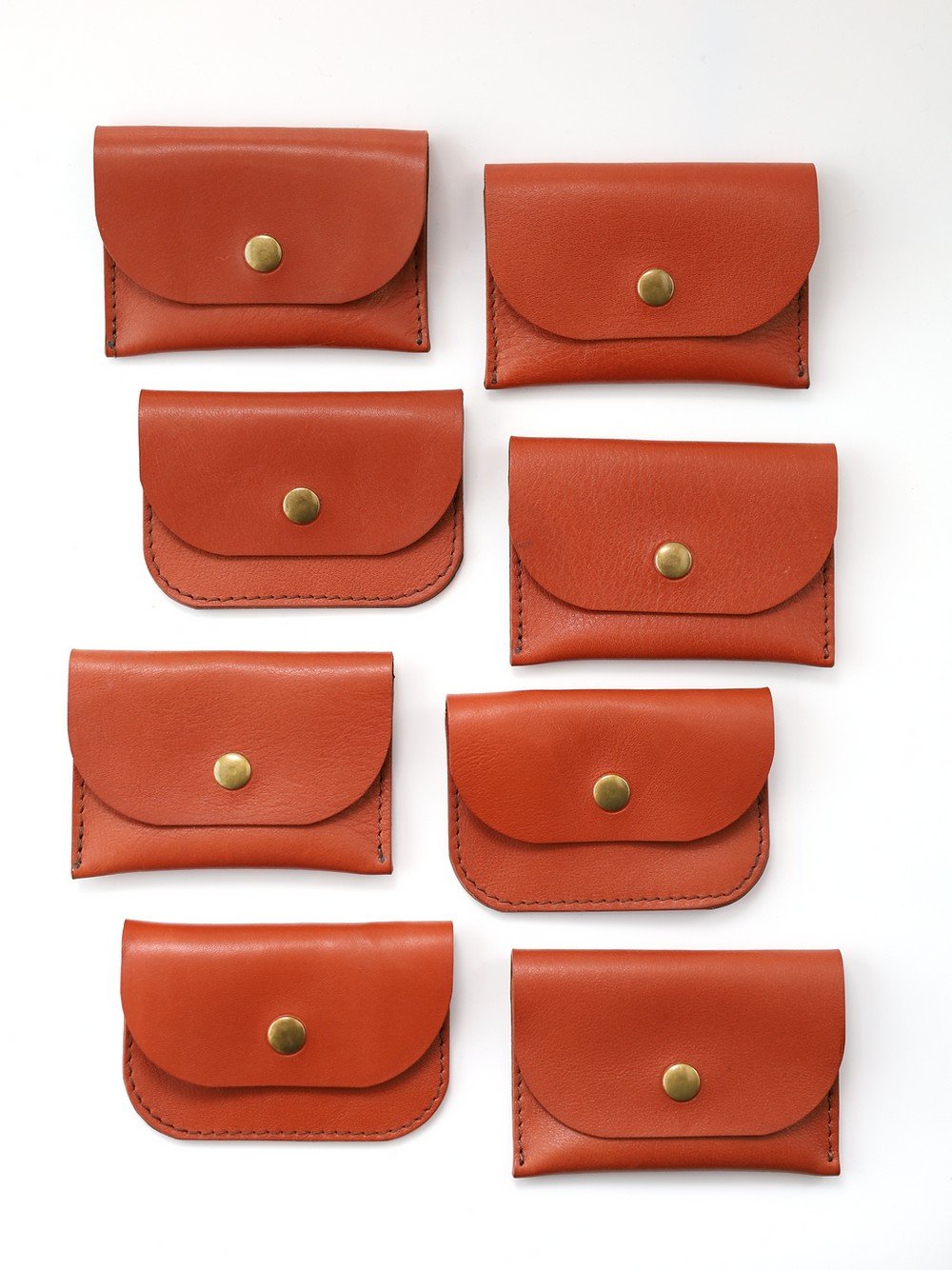 4. Flat lay of multiple red clay leather wallets by Toks Visoks with brass buttons