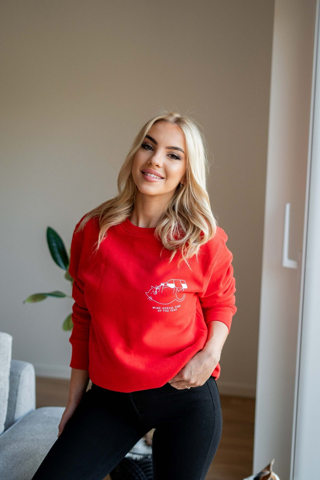 2. Woman smiling in red oversized sweatshirt with white graphic and text 'Wine-derful Time of the Year' standing in a bright room