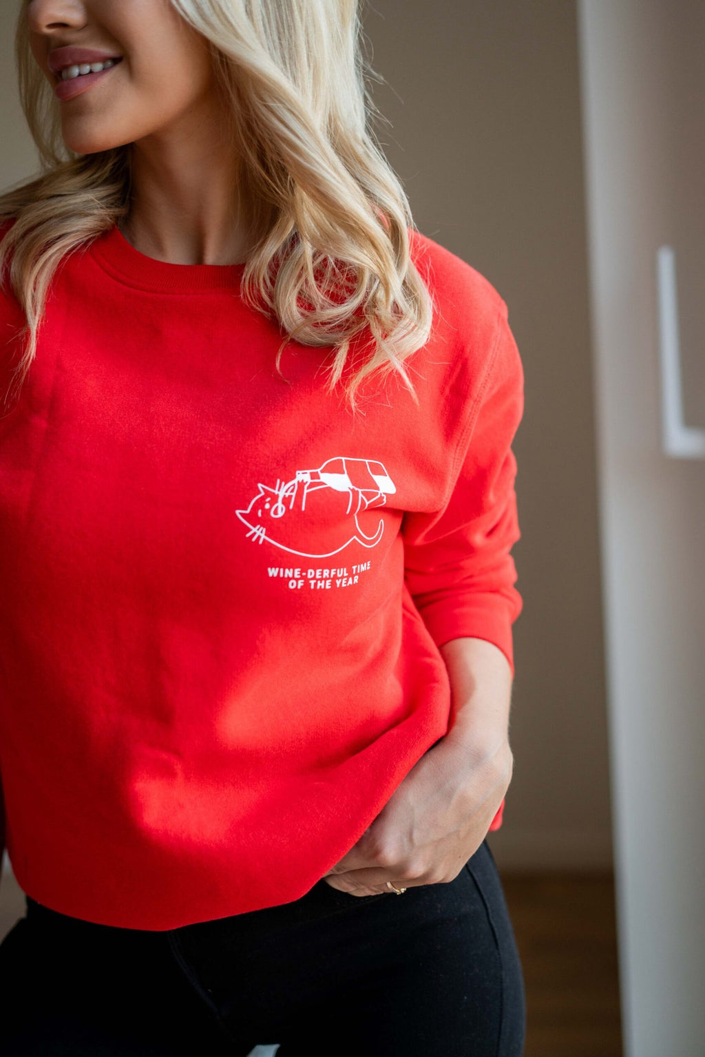 1. Woman wearing red oversized sweatshirt with white graphic and text 'Wine-derful Time of the Year' in a cozy indoor setting