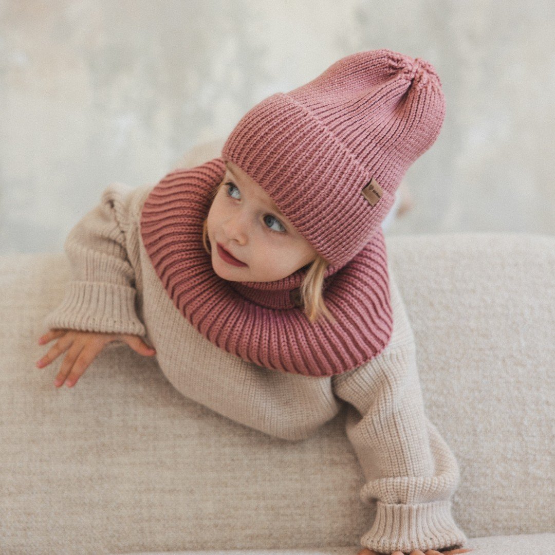 1. Child wearing blush merino wool hat and matching neck warmer on beige sofa