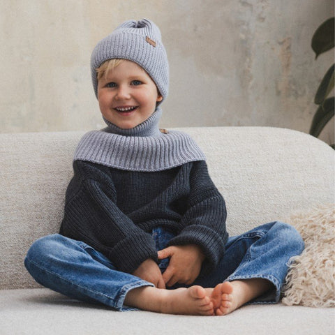 3. Child sitting on sofa wearing grey merino wool tube scarf and hat, smiling