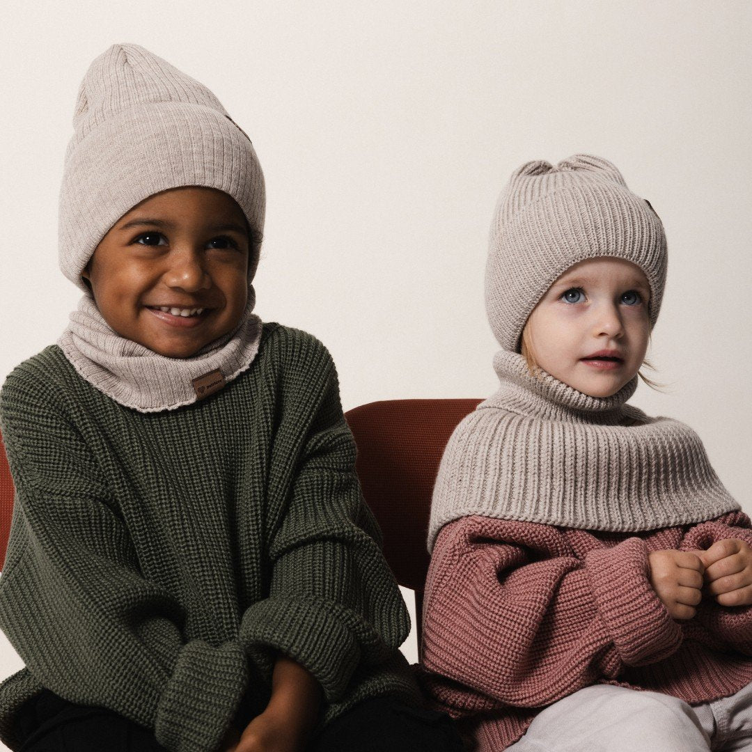 2. Two children wearing Patulove oat-colored merino wool hats and matching neck warmers, sitting indoors