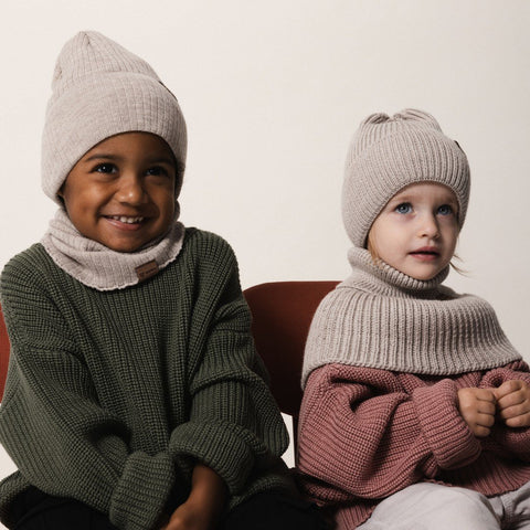 2. Two children wearing Patulove oat-colored merino wool hats and matching neck warmers, sitting indoors