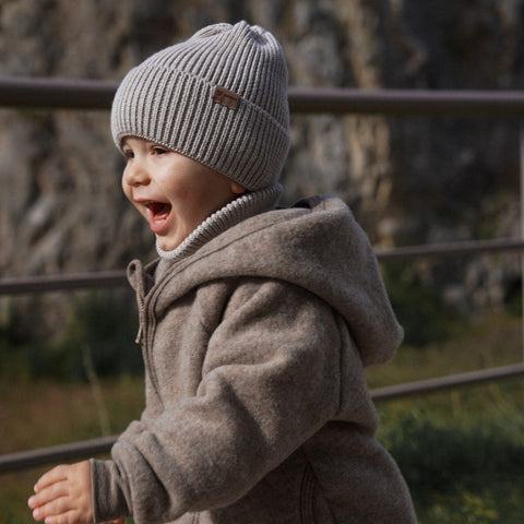 4. Smiling child wearing Patulove oat-colored merino wool hat and coat, playing outside