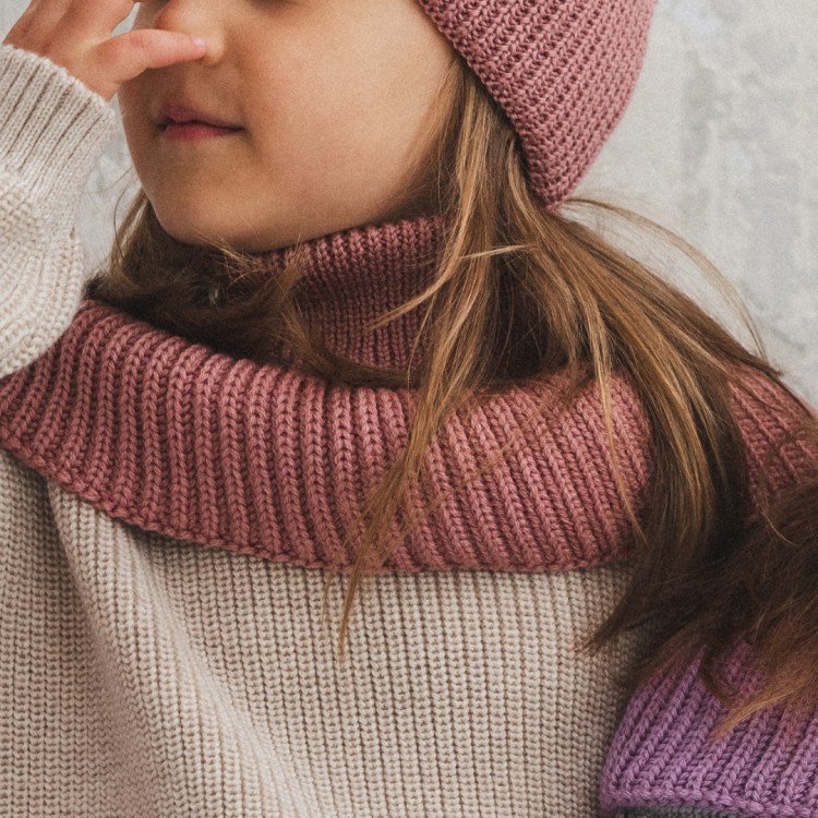 1. Girl wearing blush merino wool tube scarf and matching hat, sitting indoors with hand near face