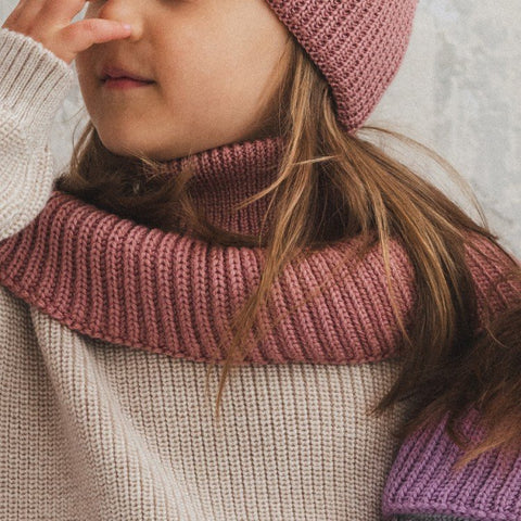 1. Girl wearing blush merino wool tube scarf and matching hat, sitting indoors with hand near face