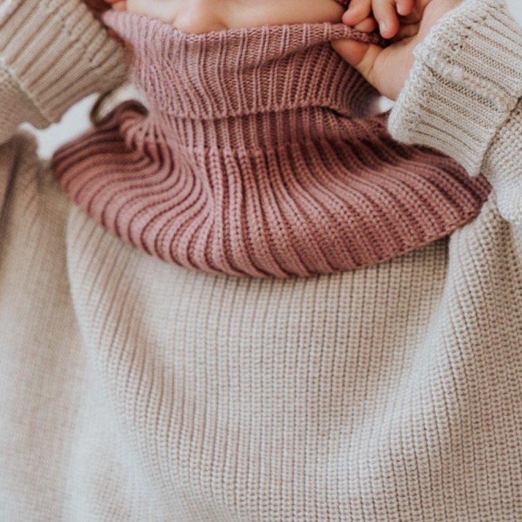 2. Child adjusting blush merino wool tube scarf, highlighting ribbed design and cozy fit