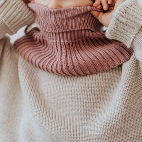 2. Child adjusting blush merino wool tube scarf, highlighting ribbed design and cozy fit