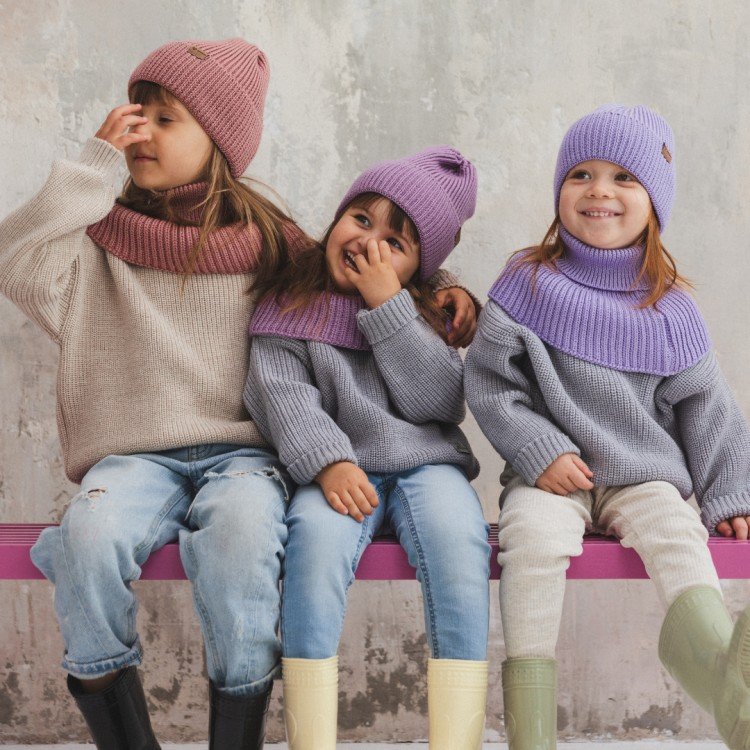 2. Three children sitting on bench wearing lavender and pink merino wool tube scarves and hats by Patulove, casual indoor setting