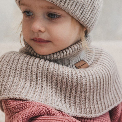 1. Child wearing oat-colored merino wool tube scarf and matching hat, sitting indoors with a soft expression