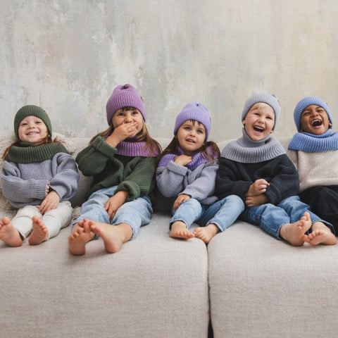 2. Group of five children sitting on a couch wearing colorful merino wool tube scarves and hats, smiling and laughing