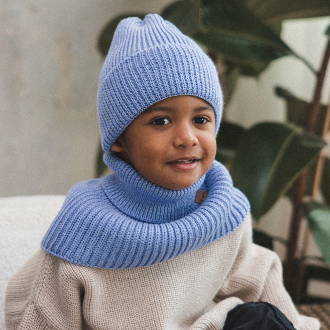 4. Child smiling in sky blue merino wool tube scarf and hat by Patulove, sitting indoors