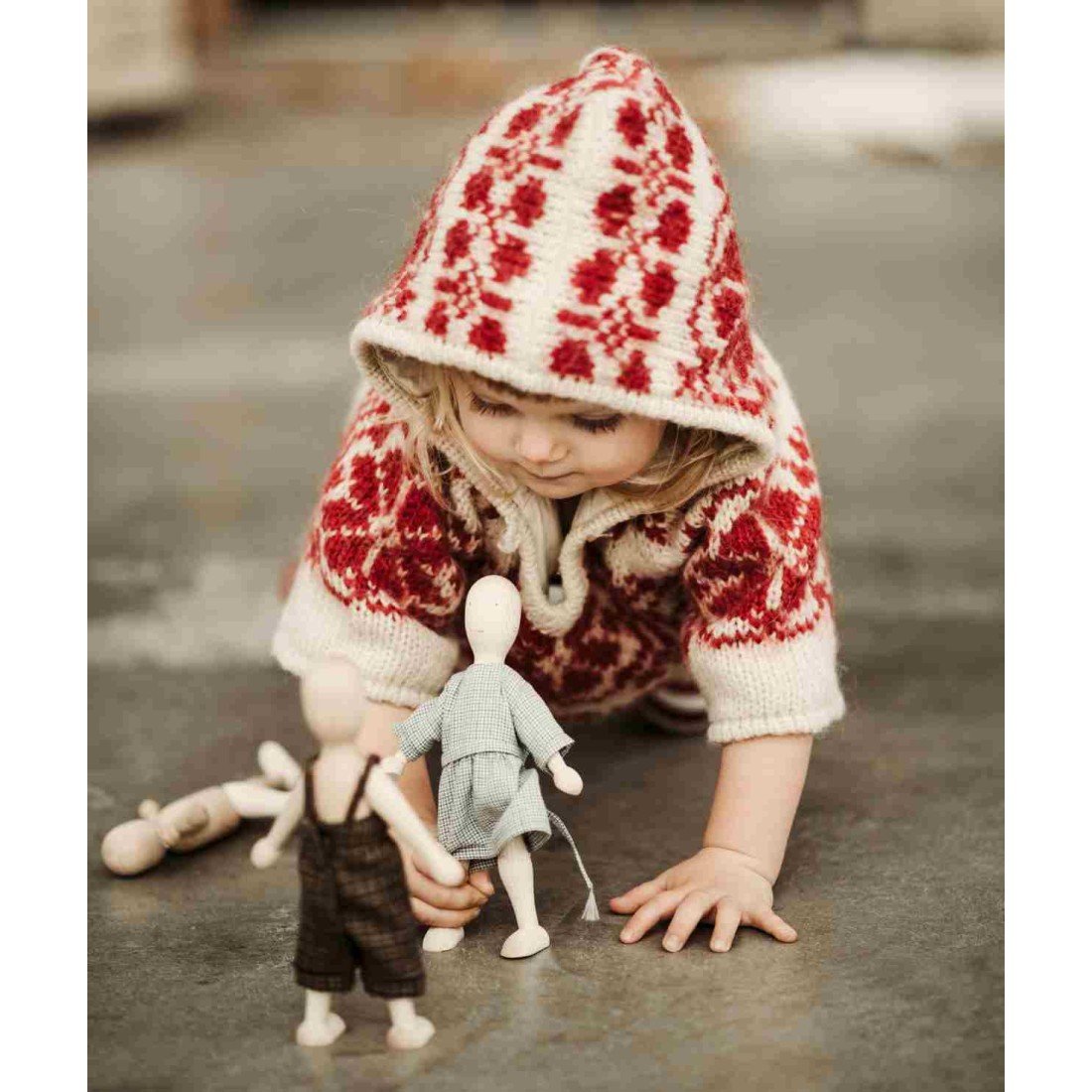 1. Child in red patterned hoodie playing with Wooden Story dolls on a concrete floor