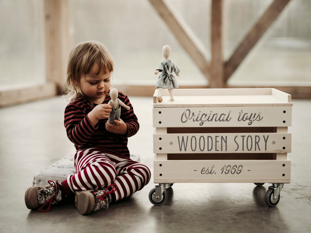 2. Child in striped pajamas playing with Wooden Story beech doll next to branded wooden crate