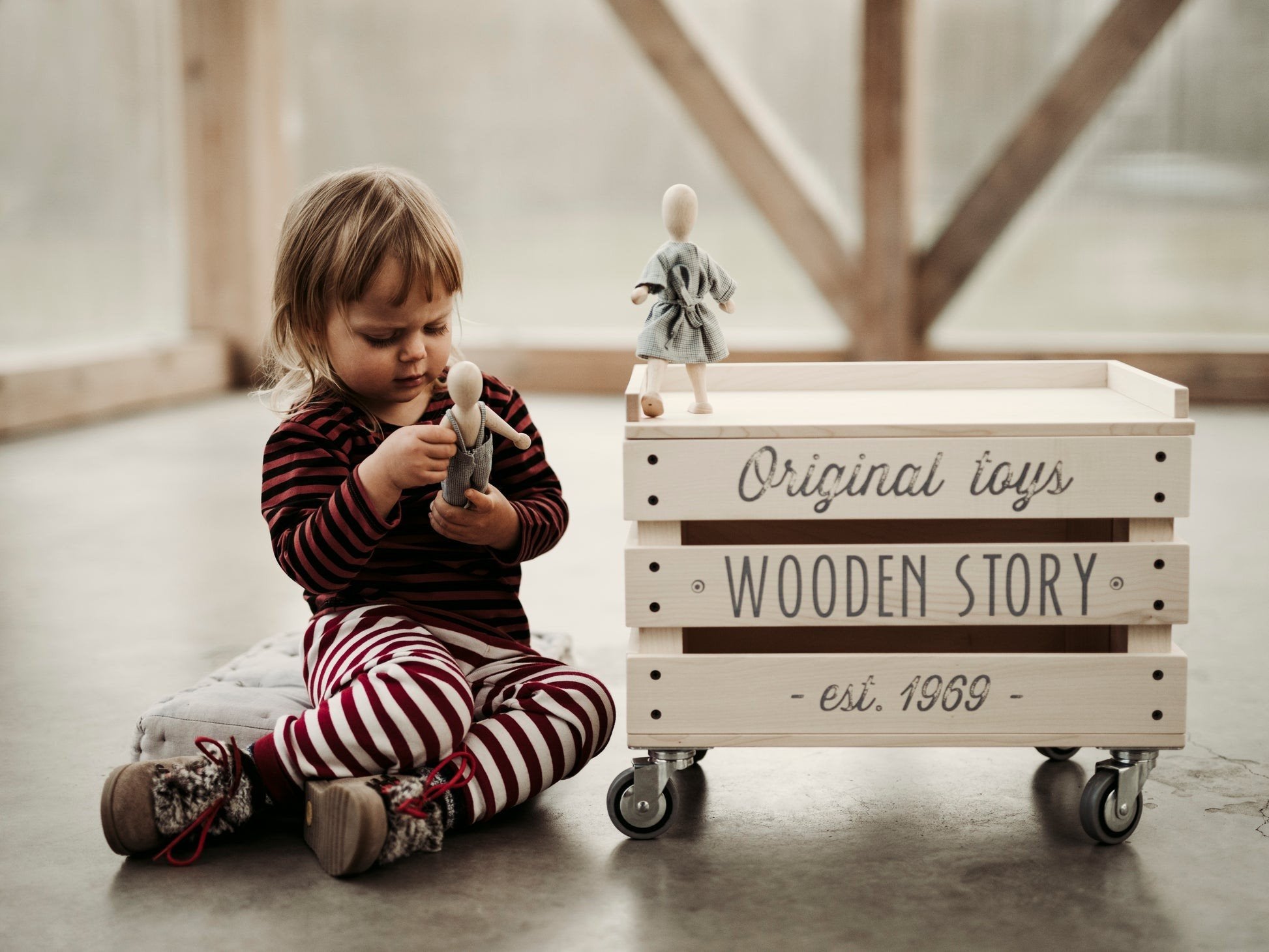 2. Child in striped pajamas playing with Wooden Story beech doll next to branded wooden crate