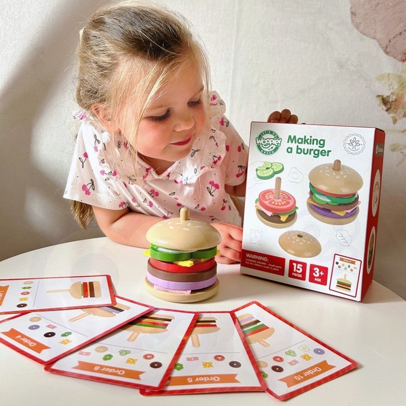 9. Girl playing with wooden burger puzzle set and recipe cards, with packaging box on a table