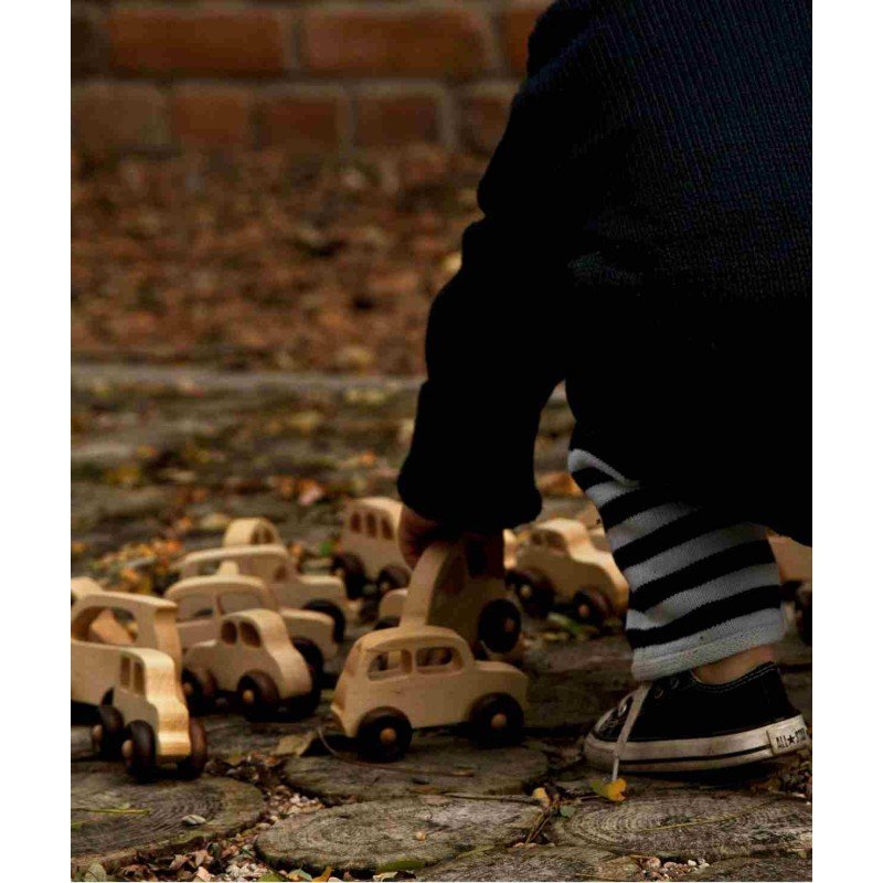1. Child arranging Wooden Story wooden cars on a cobblestone path, wearing striped pants and sneakers