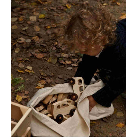 1. Child placing Wooden Story toy cars into a cloth bag on a leafy ground