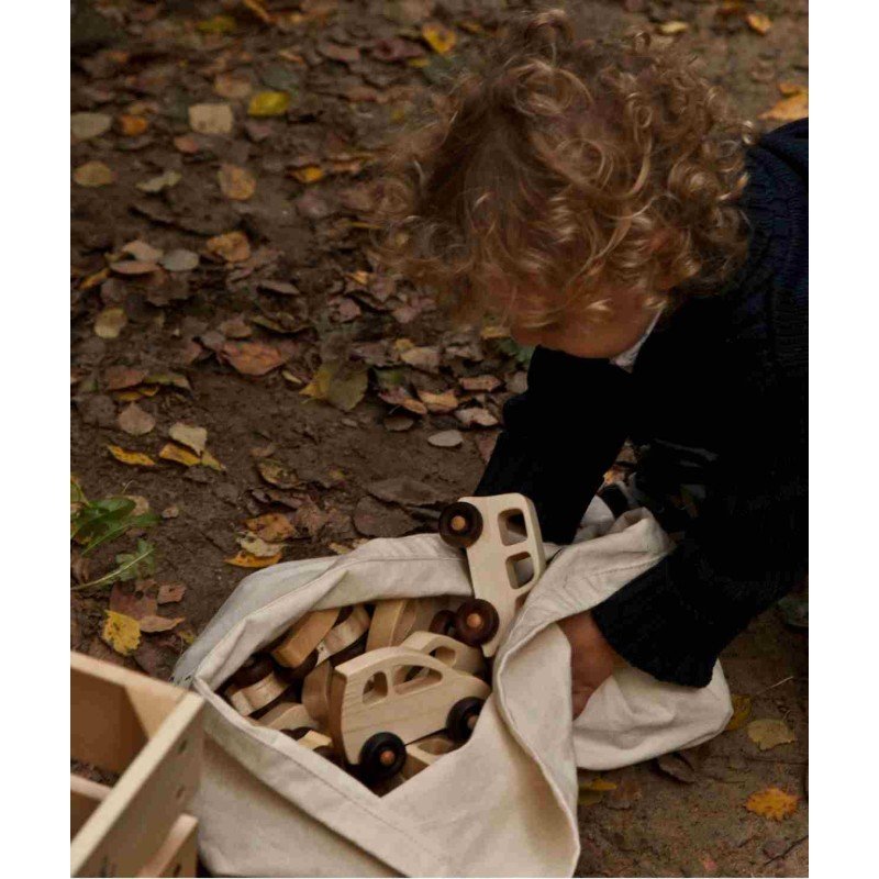4. Child with curly hair playing with Wooden Story toy cars in a fabric bag on a leafy ground