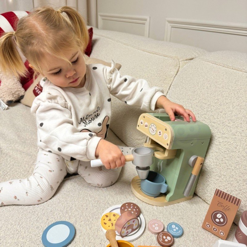 1. Child using Woopie Green coffee machine with pastries and cups on sofa