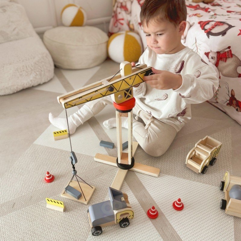 14. Child using Woopie Green wooden crane and vehicles on a carpet