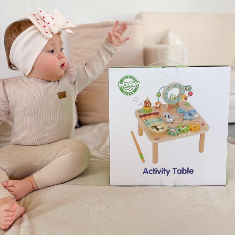 15. Toddler reaching for Woopie 5-in-1 activity table box on beige sofa
