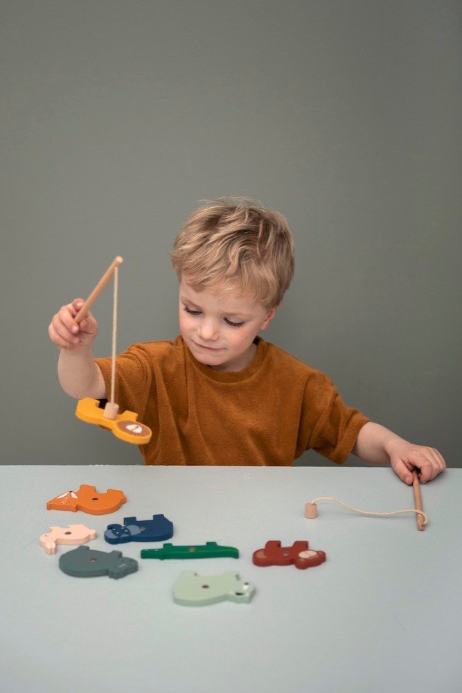 1. Child playing with Trixie Baby wooden fishing game, holding rod with animal piece, on light green background