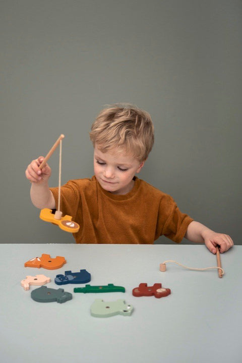 1. Child playing with Trixie Baby wooden fishing game, holding rod with animal piece, on light green background