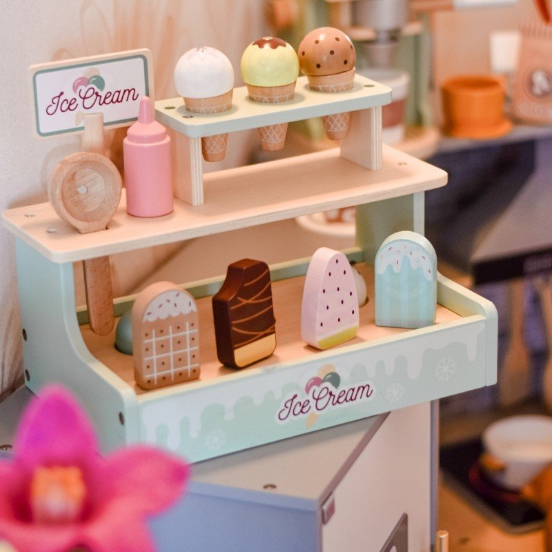 1. Child playing with Woopie Green wooden ice cream stand, featuring colorful cones and popsicles in a cozy room setting