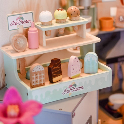 1. Child playing with Woopie Green wooden ice cream stand, featuring colorful cones and popsicles in a cozy room setting